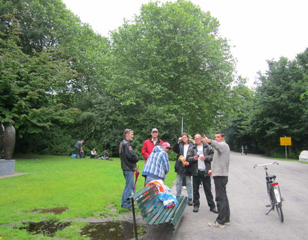 Dak- en thuislozen in het Oosterpark. Een biertje gaat er altijd wel in. Op de achtergrond zitten er een paar in het kletsnatte gras.