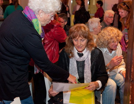 Vrijwilligers Annielies Griffioen en Elly van Mourik bespreken oude foto's van Buurtwinkels die zij verzameld hebben.